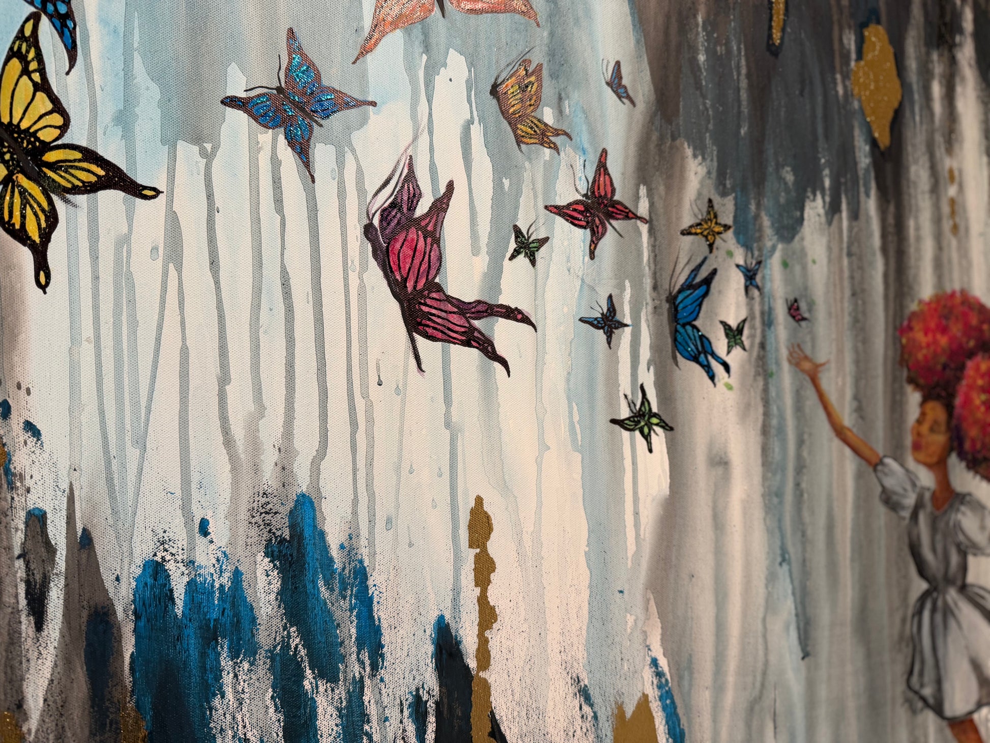 Abstract wall art featuring colorful butterflies flying over a textured background with blue, gray, white, and gold paint drips, alongside a painted figure on the right.