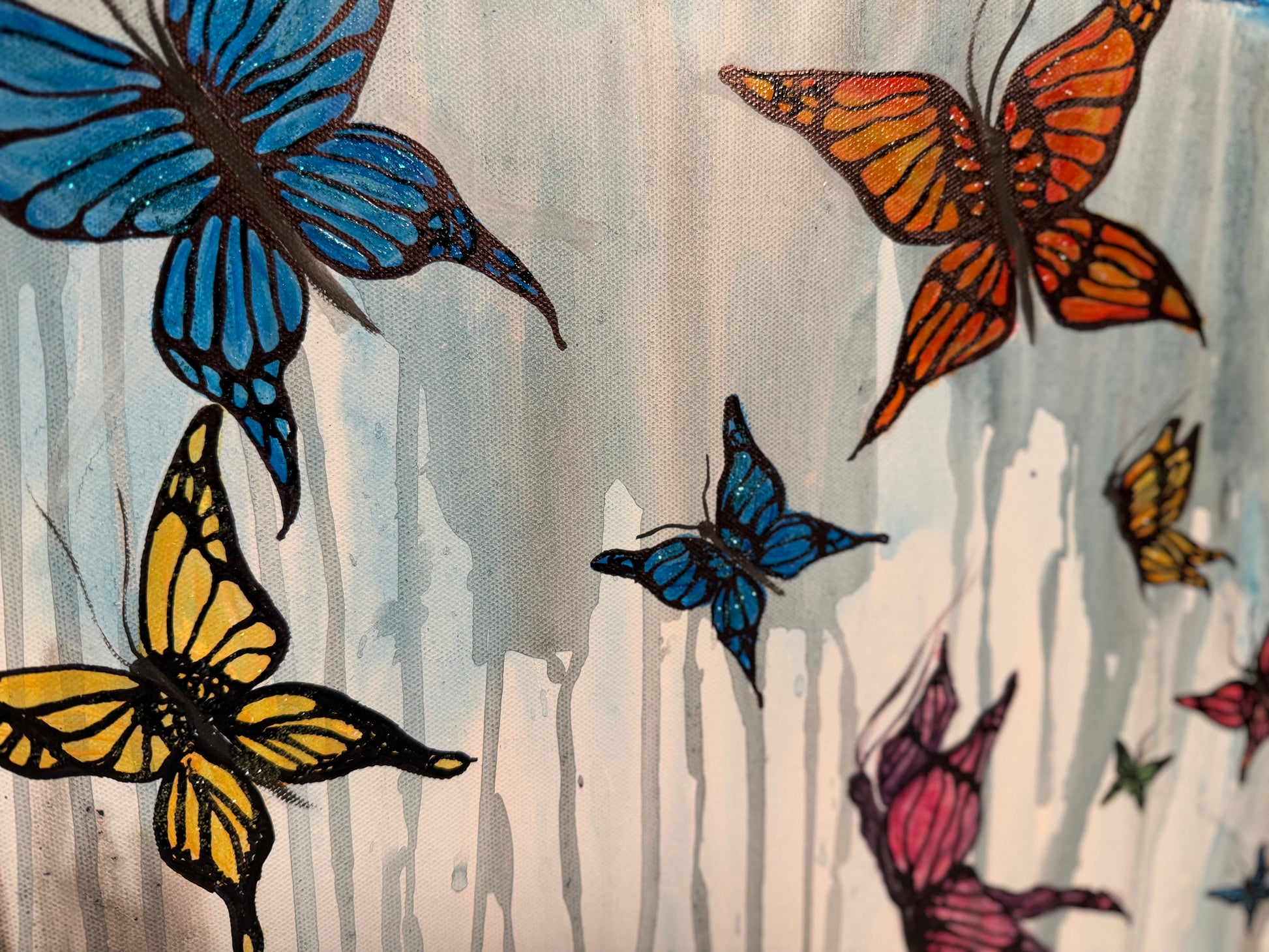 A close-up of a painted butterfly pattern on a light gray and white textured background, featuring several large and small butterflies in blue, orange, yellow, pink, and black outlines.
